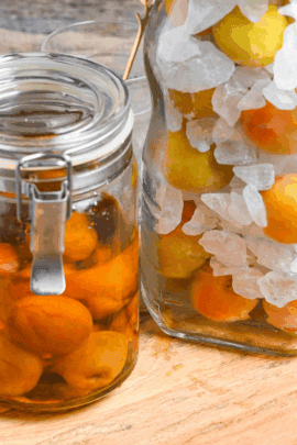 completed ume syrup in a jar next to a jar of ume and rock sugar in layers on a wooden board