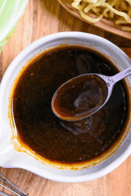 Homemade yakisoba sauce in a small white ceramic jug with silver spoon held above